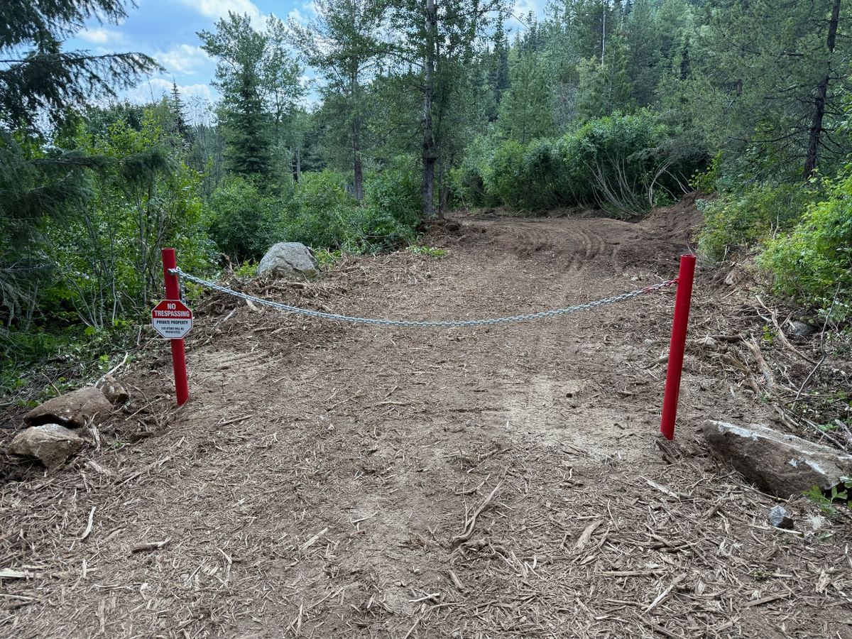 Remote mountain access road built into steep timbered banks in Samuels, Idaho by Premier Land Service, with red bollards and lockable chain gate at the private entrance.