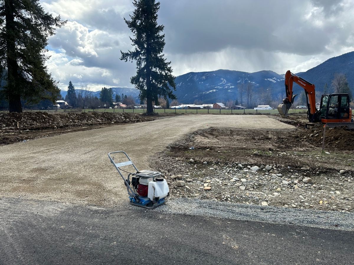 New shop building pad graded and compacted with plate compactor and Hitachi excavator in Clark Fork, Idaho — Premier Land Service site prep with mountain backdrop.