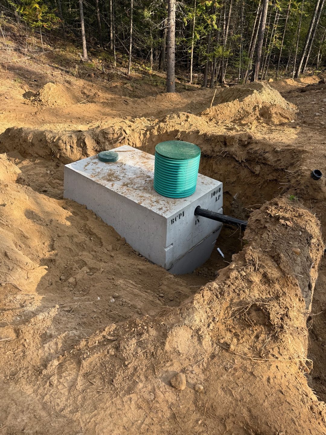 Residential 1000-gallon septic tank set in excavated pit with riser and inlet plumbed for a cap-and-fill drainfield install in Sagle, Idaho by Premier Land Service.