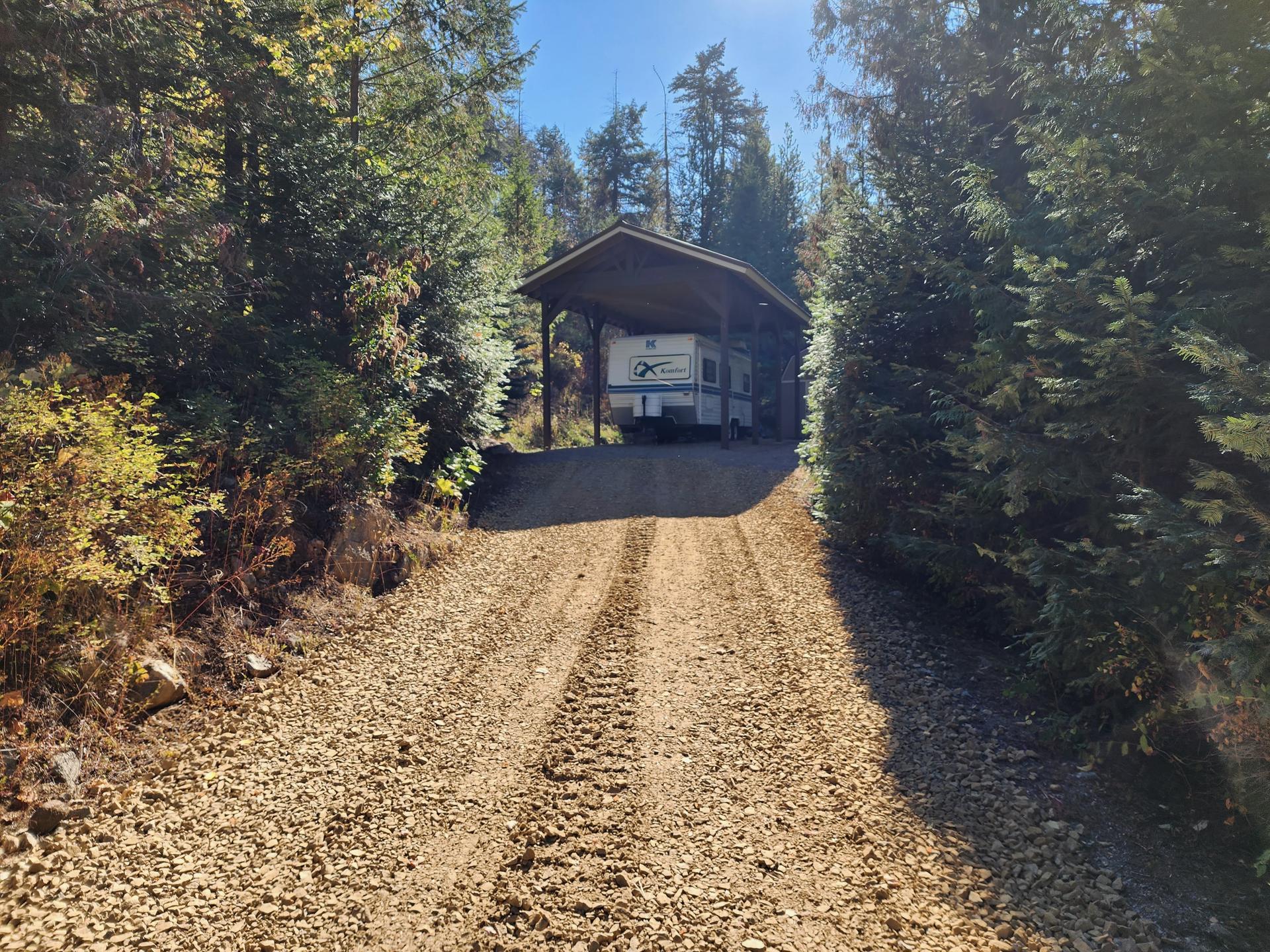 Freshly graded gravel driveway leading to covered structure through pine forest