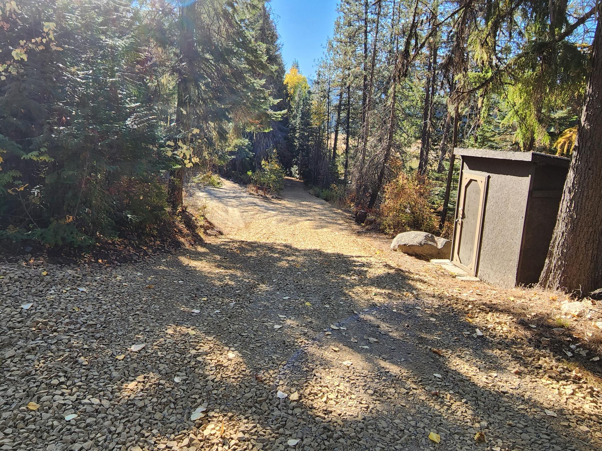 Premier Land Service gravel driveway through evergreen forest with portable toilet