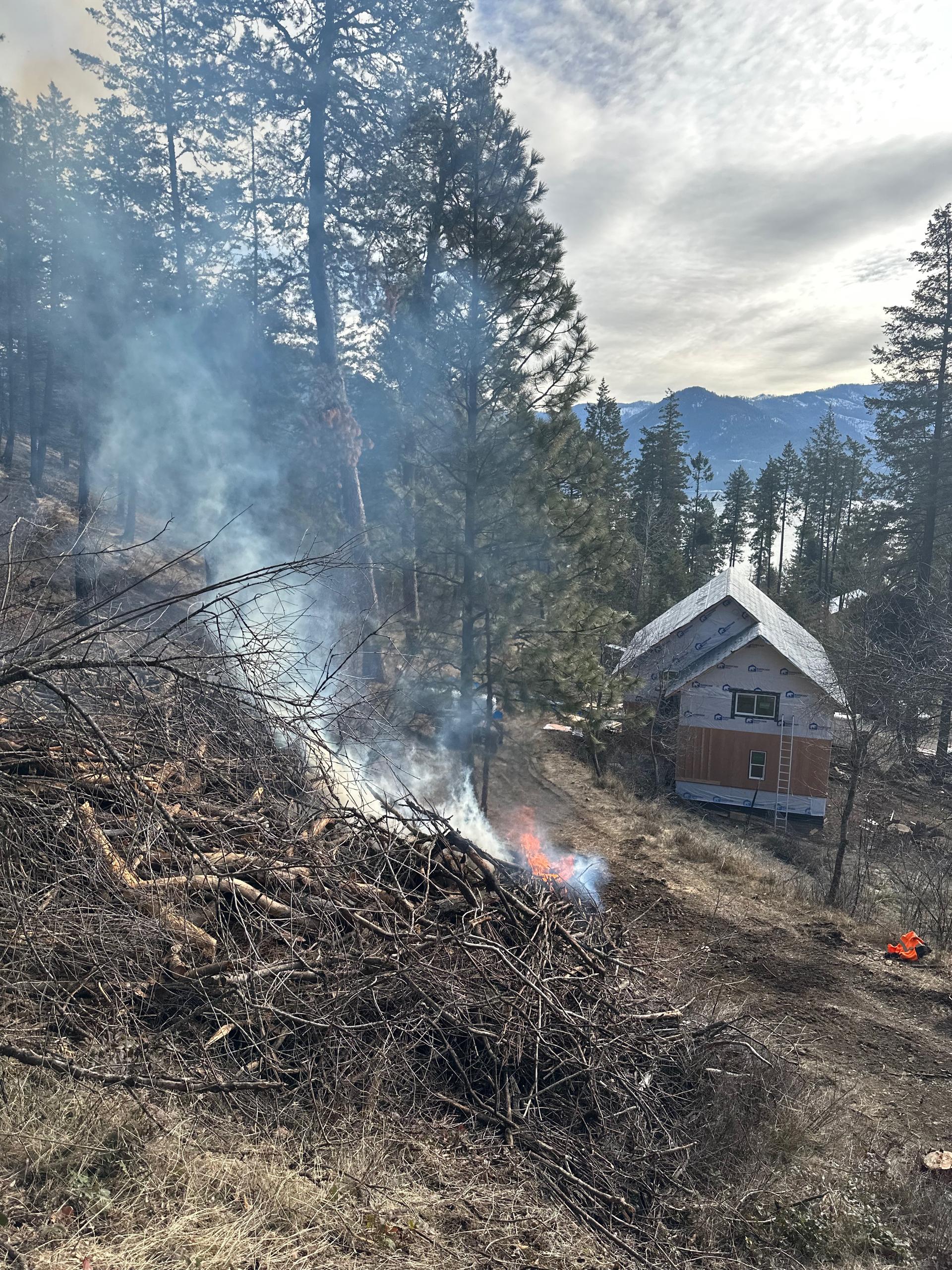 Slash burn pile smoking near cabin during fire fuels mitigation project