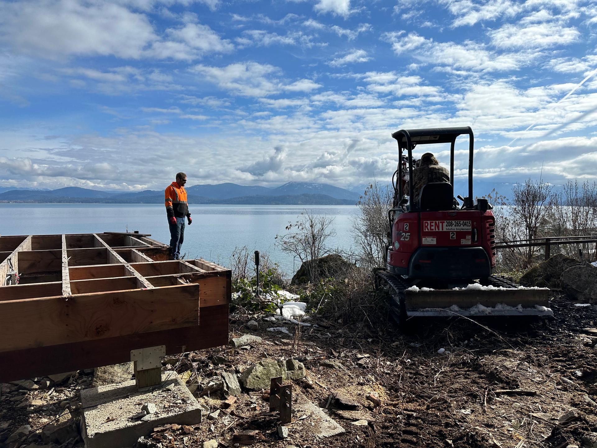 Kubota excavator digging near lakeside with crew on demolition project