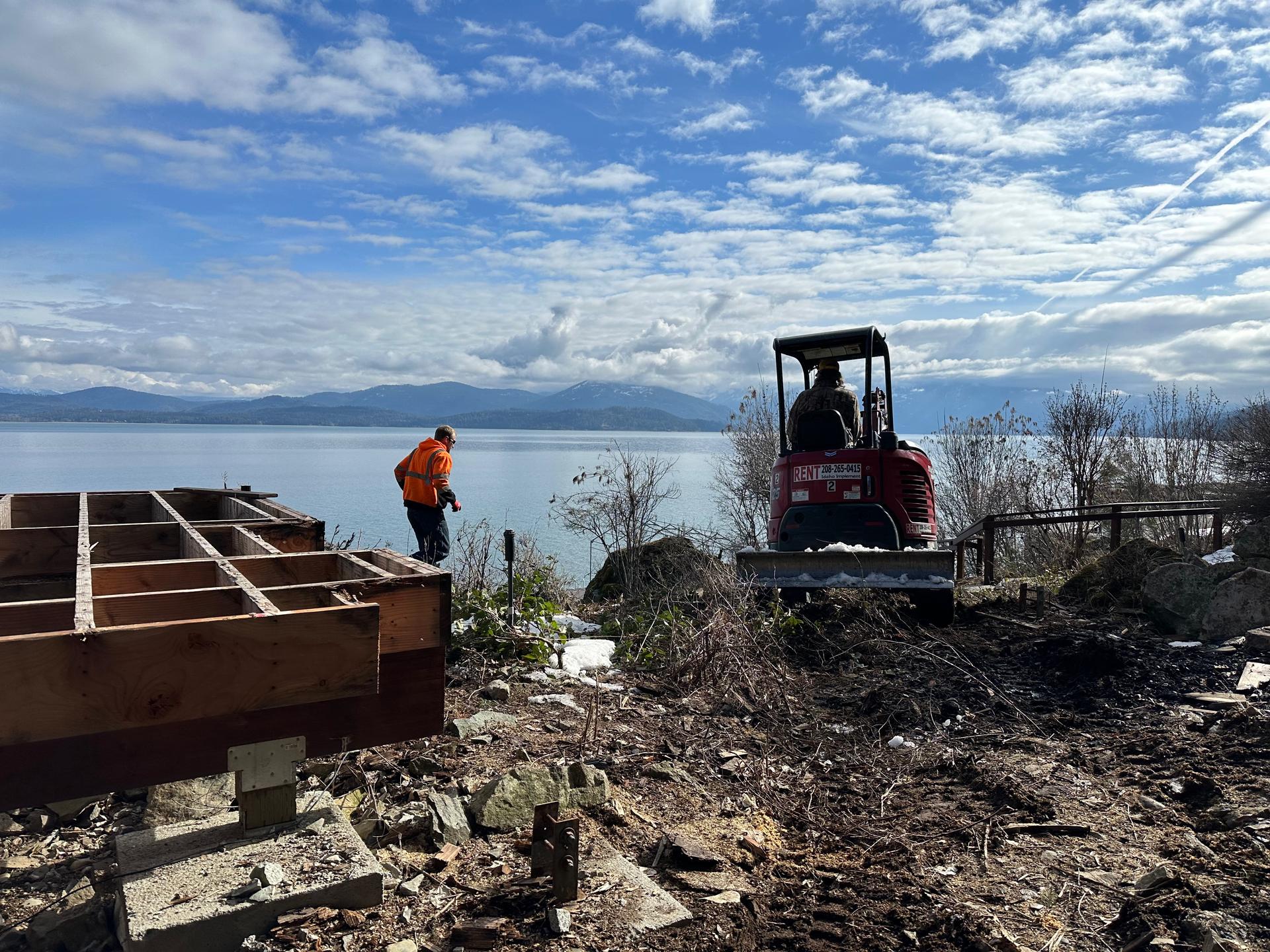 Mini excavator working lakefront excavation with workers and winter conditions