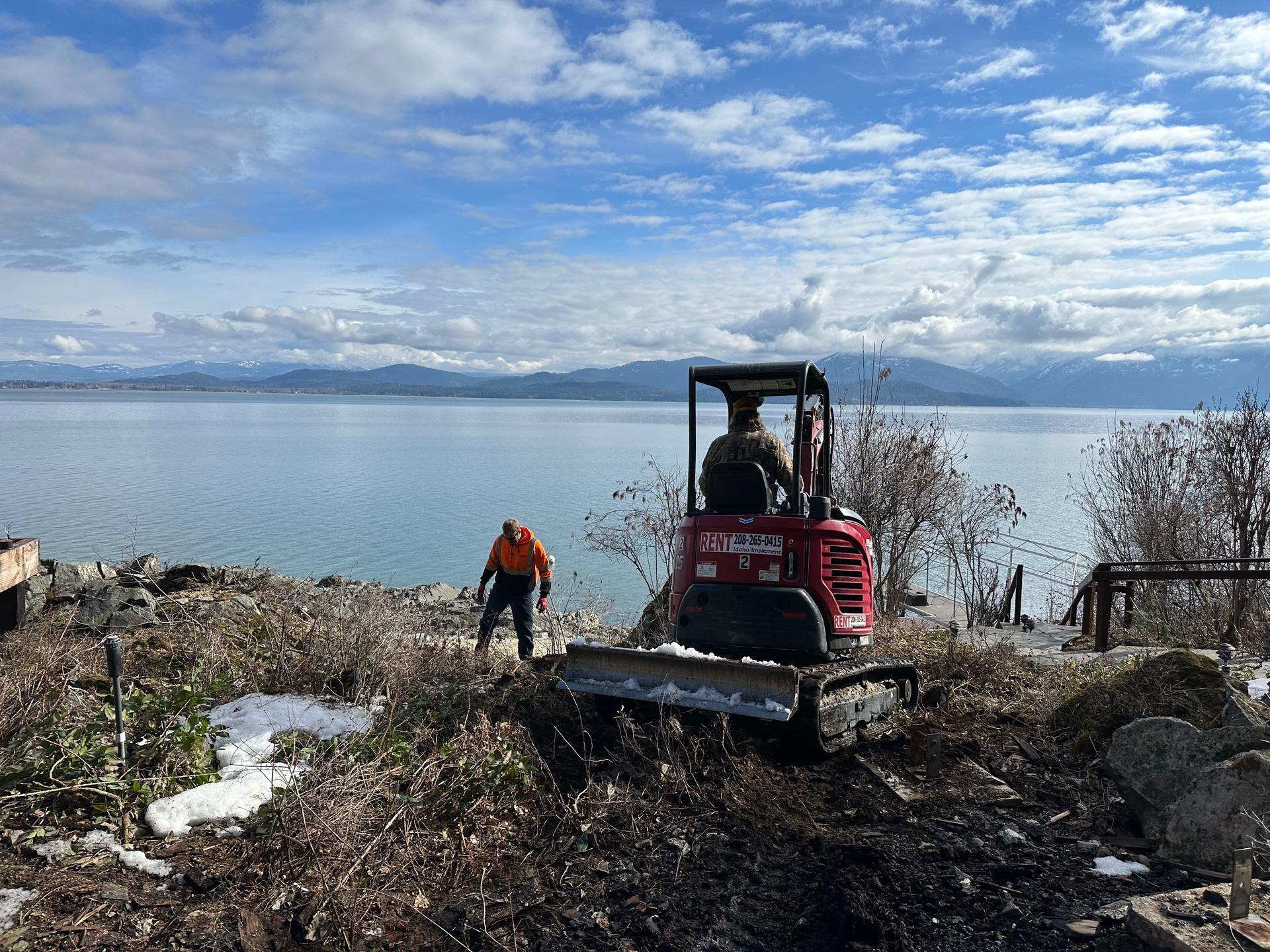 Excavator working lake shoreline site prep with Pend Oreille Lake in background
