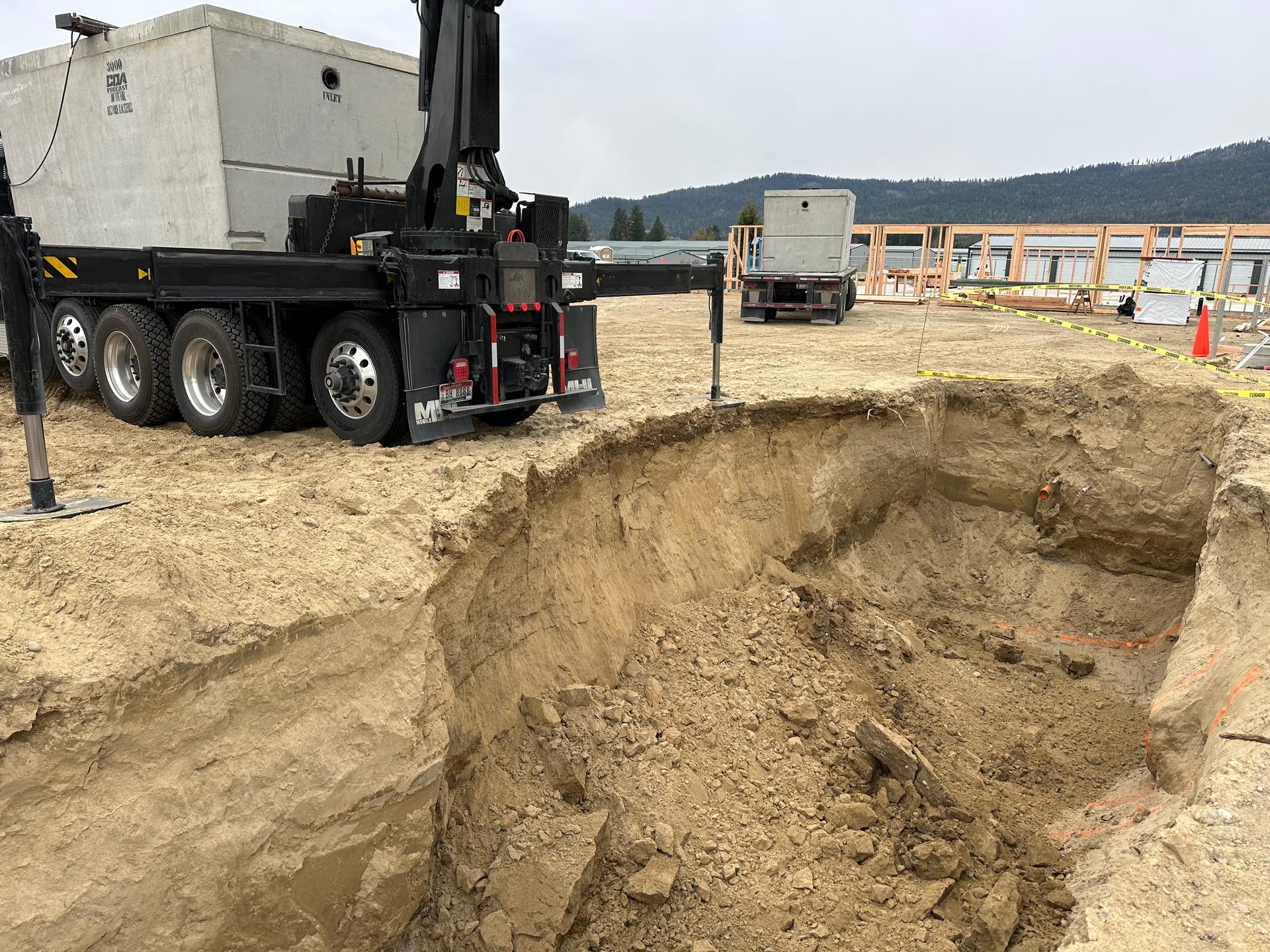 Crane truck lowering concrete septic tank into large excavated pit