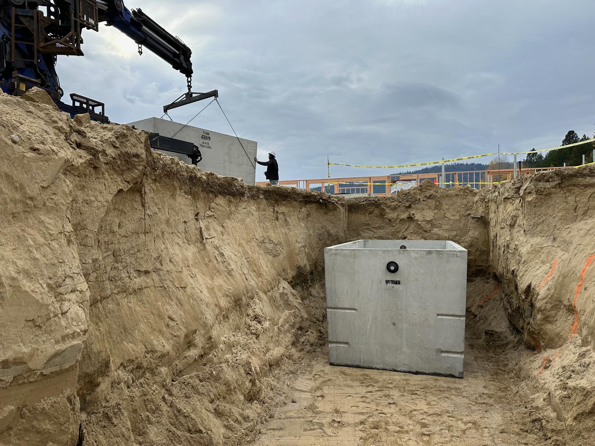 Concrete septic tank being crane-set into excavated pit at large subdivision project