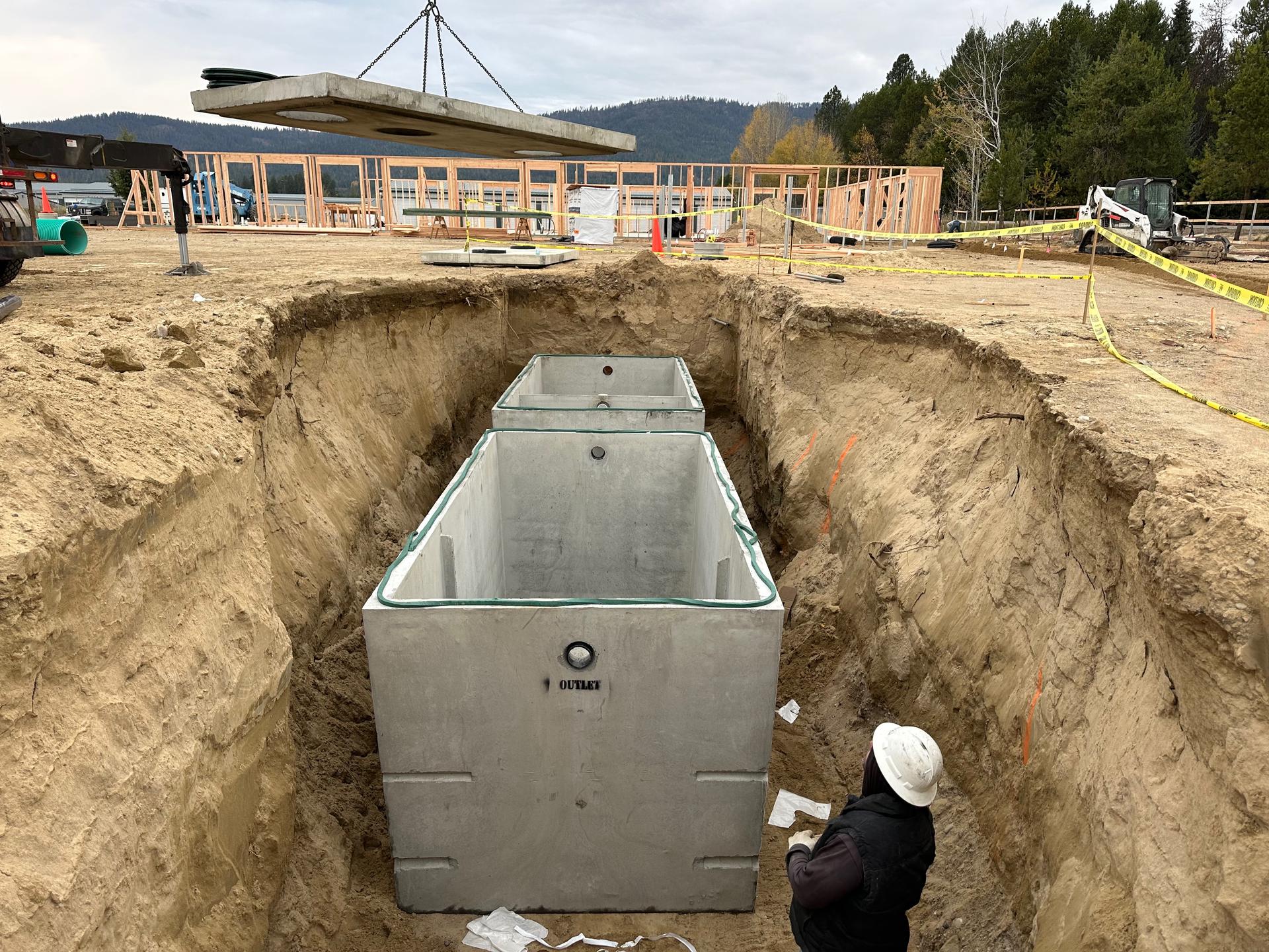 Large concrete septic tank in excavated trench with worker for scale