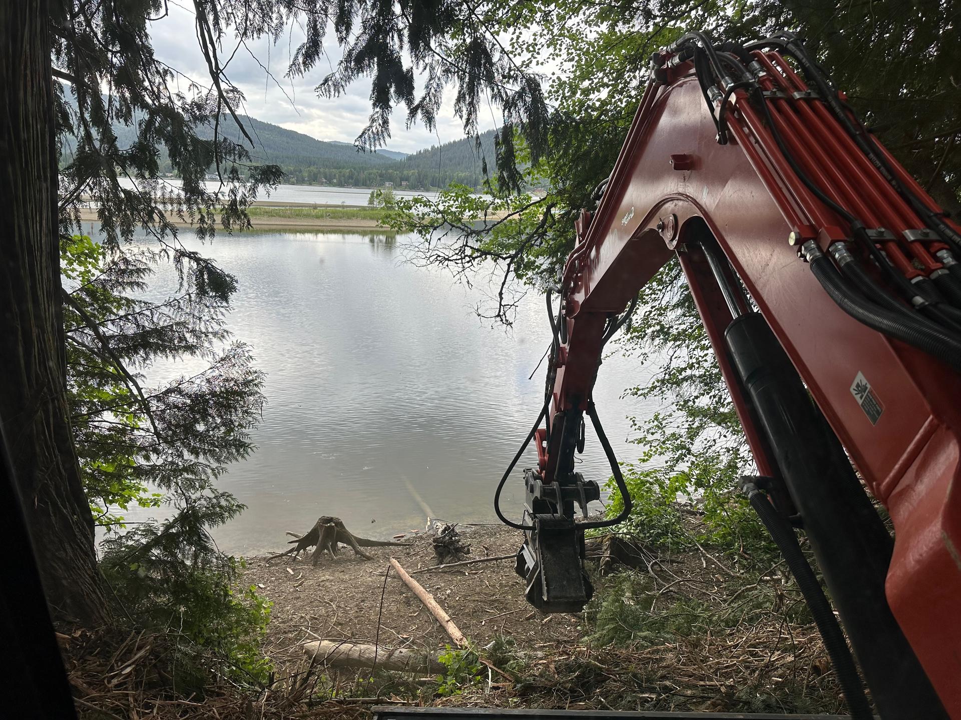 Mini excavator working near pond edge with excavator boom and water view