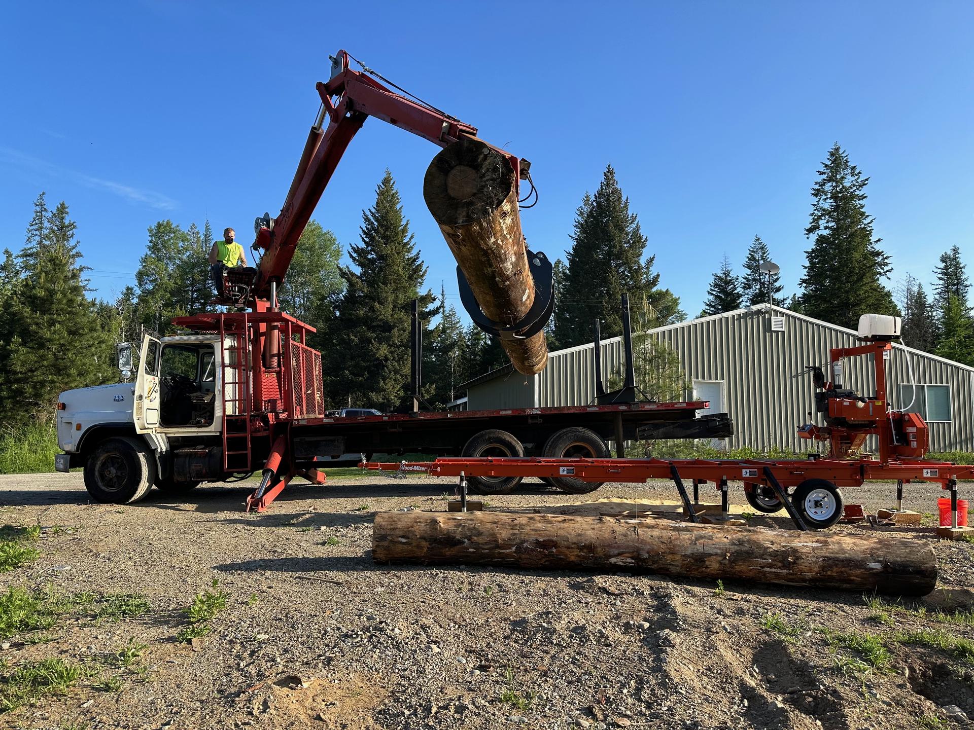 Log loader crane truck lifting timber at Premier Land Service operation blue sky