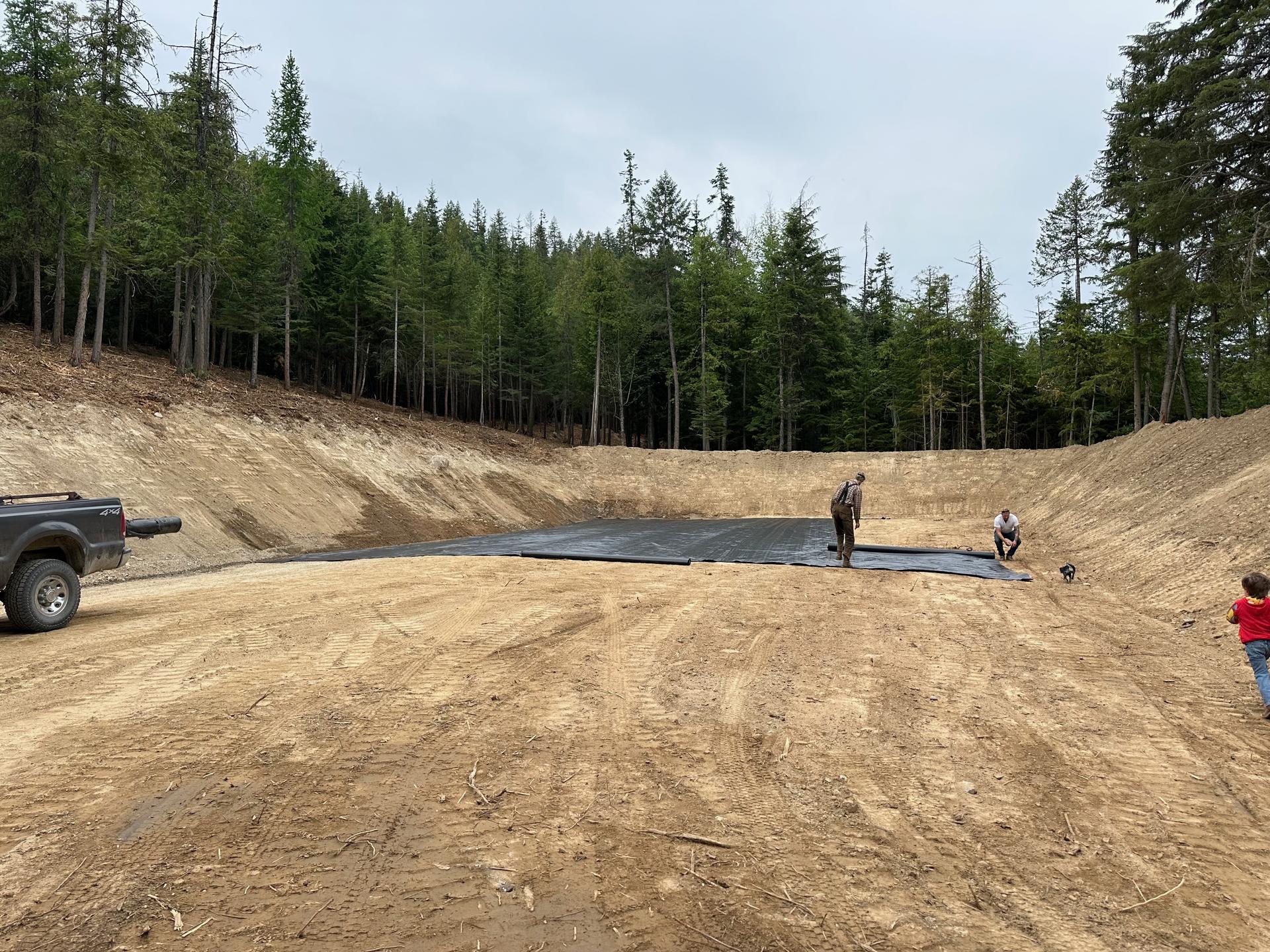 Wide angle view of large graded site with geotextile liner installation crew