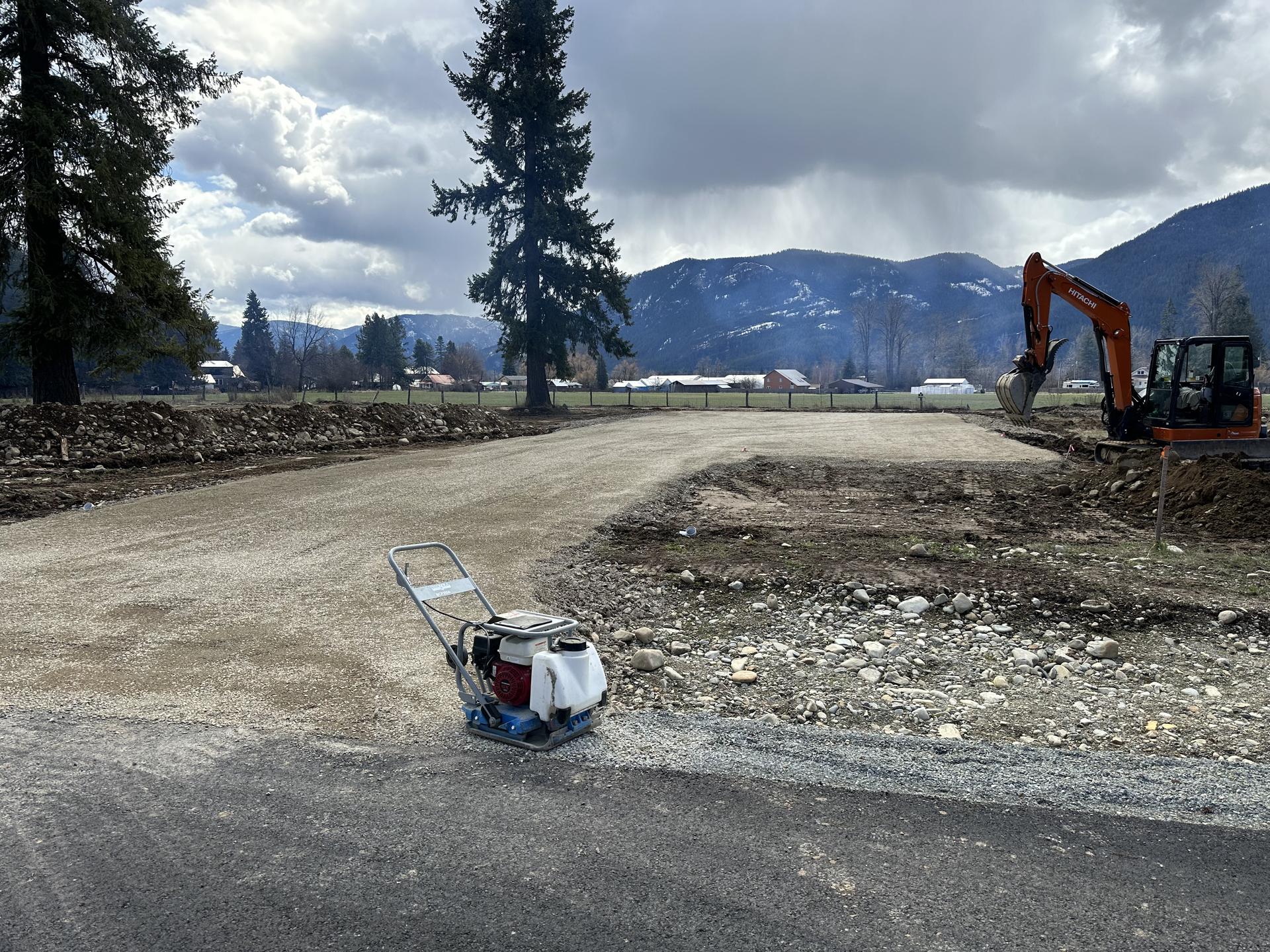 Plate compactor finishing gravel driveway with excavator and Sandpoint mountains