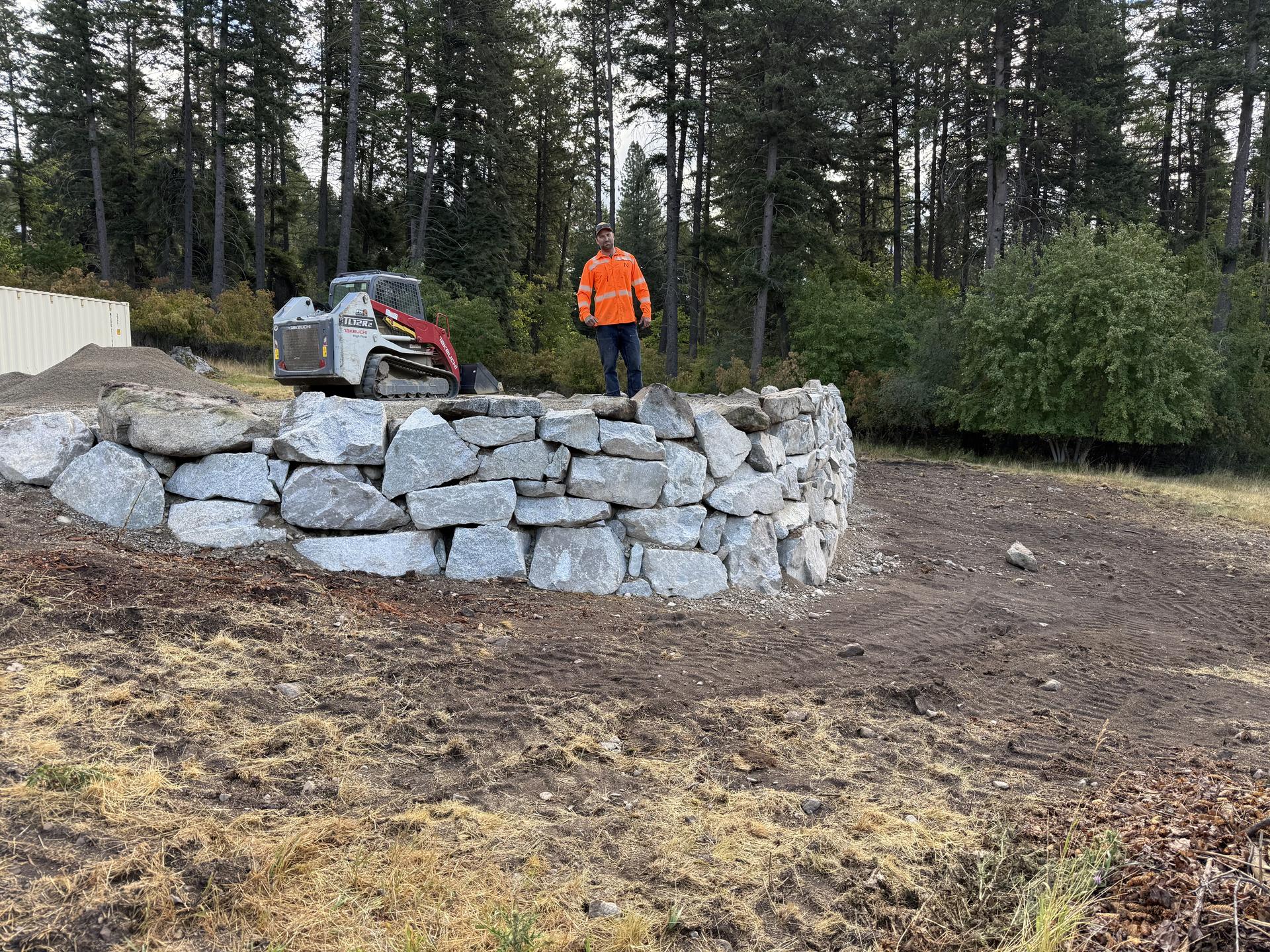 Long grey boulder retaining wall across a cleared slope