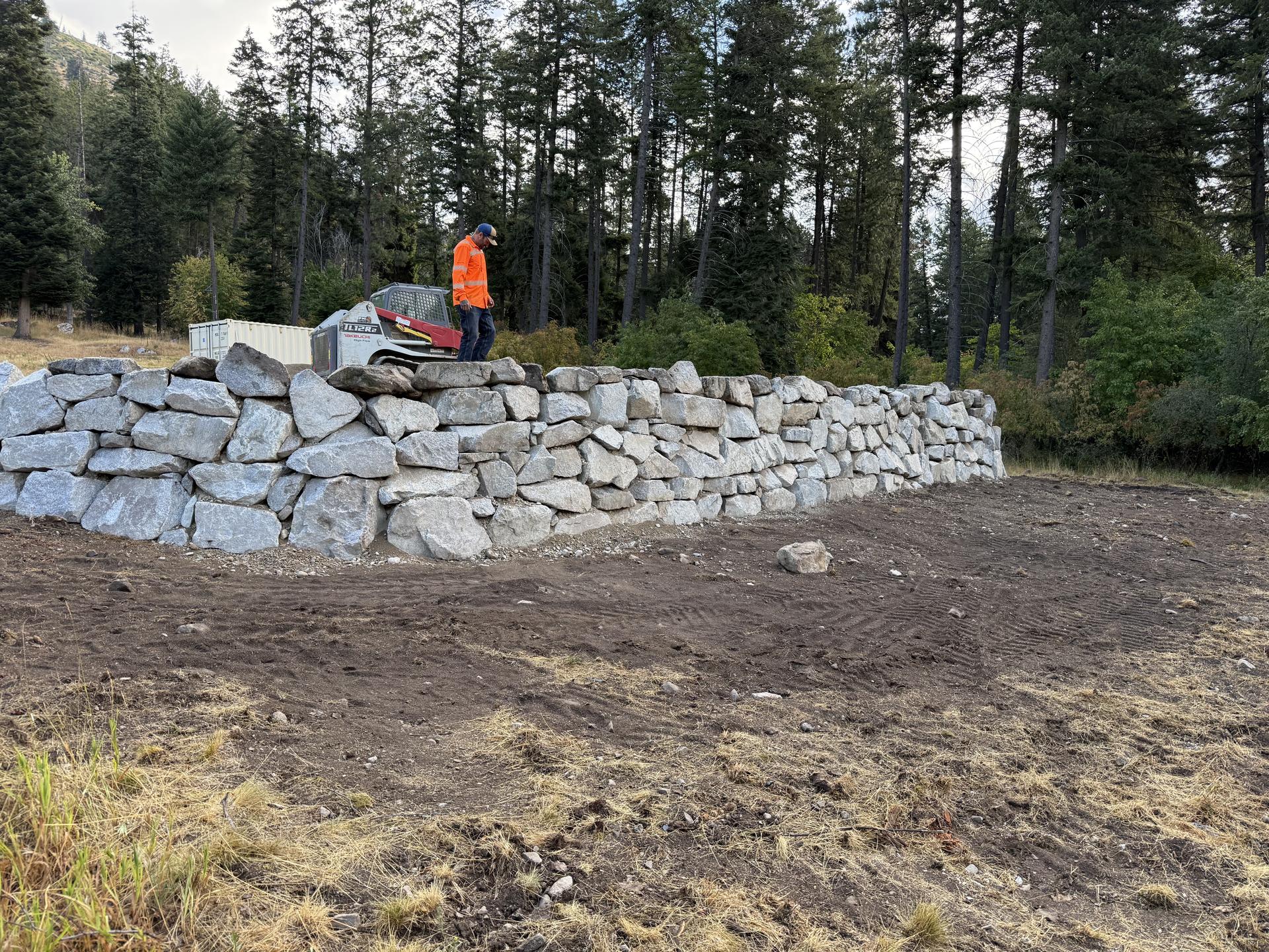 Premier Land Service long boulder retaining wall on cleared slope mountain backdrop