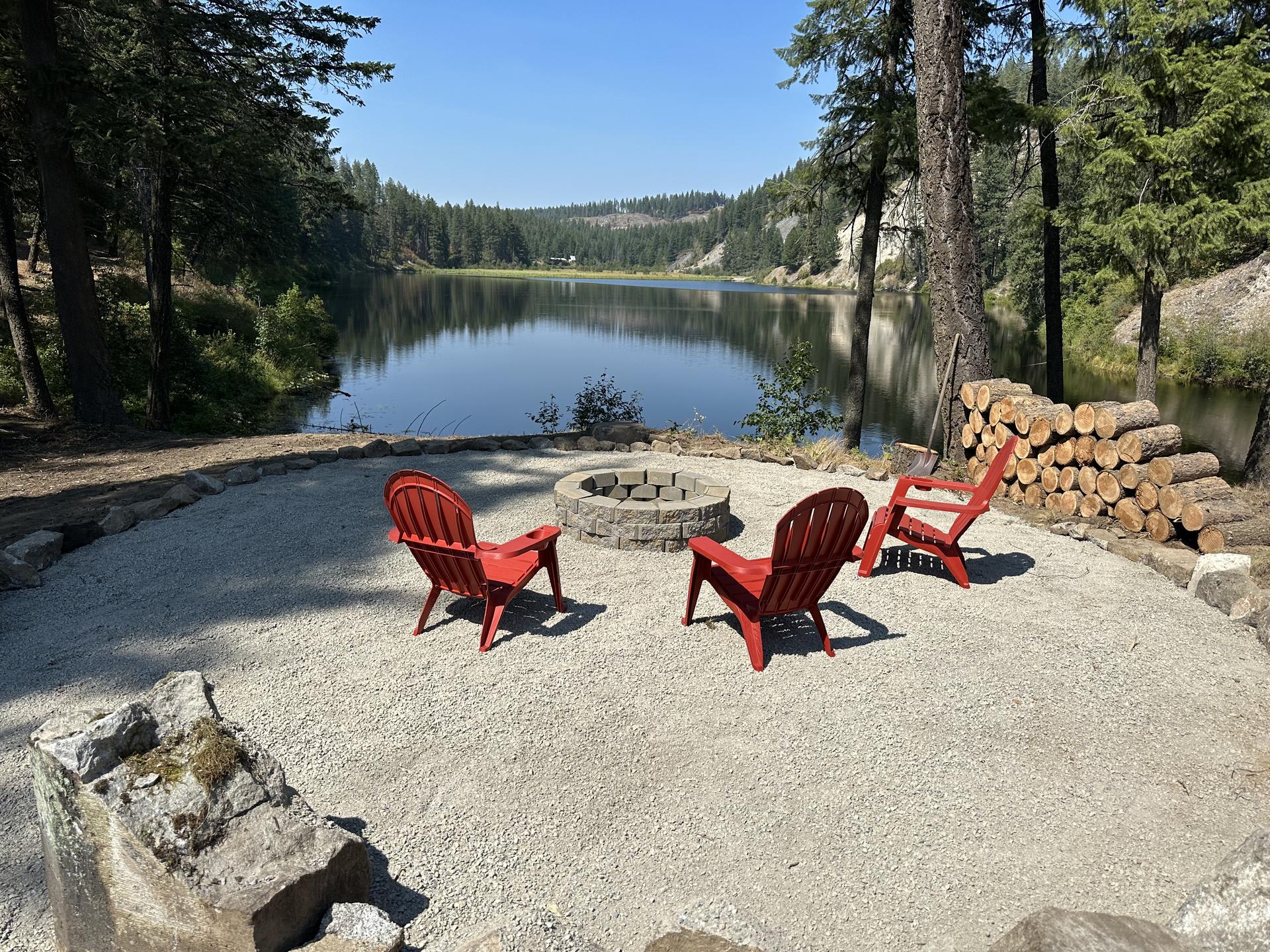Red Adirondack chairs at lakefront fire pit with mountain view