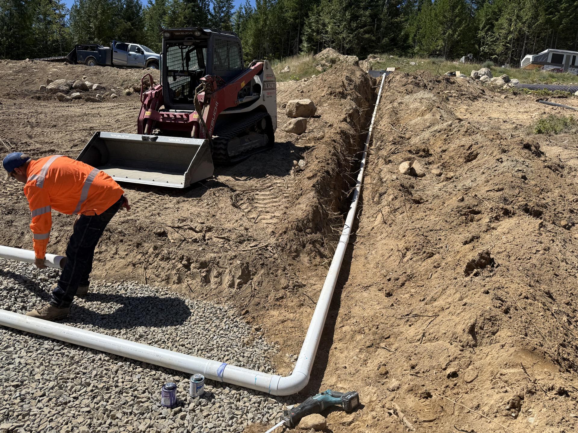 Premier Land Service crew installing drain pipe with skid steer in forest