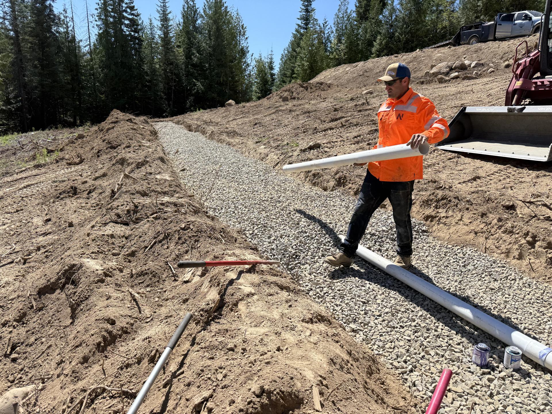Worker handling drain field pipe with skid steer helping at Premier Land Service