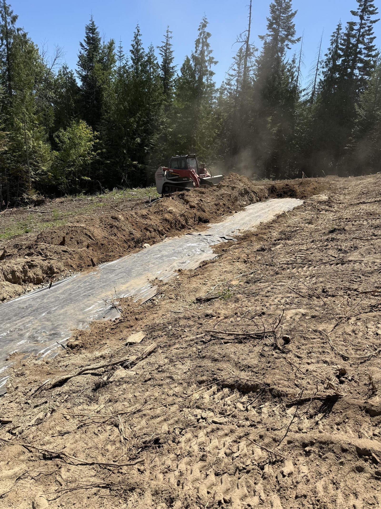 Gravel road compaction with plate tamper and excavator with Sandpoint lake view