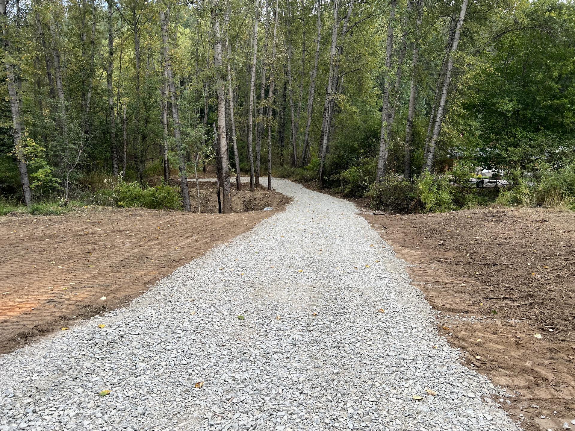 Premier Land Service finished white gravel driveway with excavator in background forest