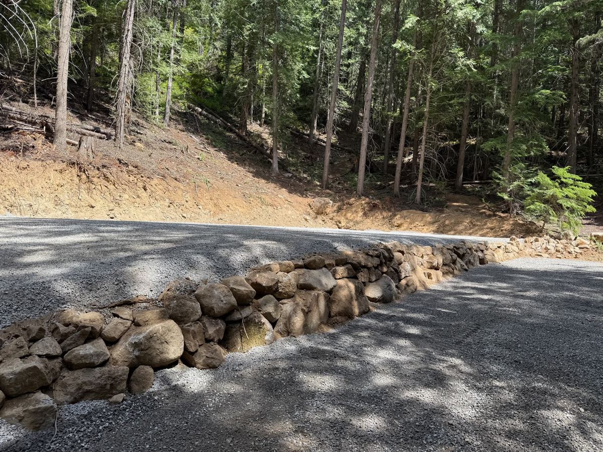 Native-rock boulder retaining wall along a newly graded gravel drive