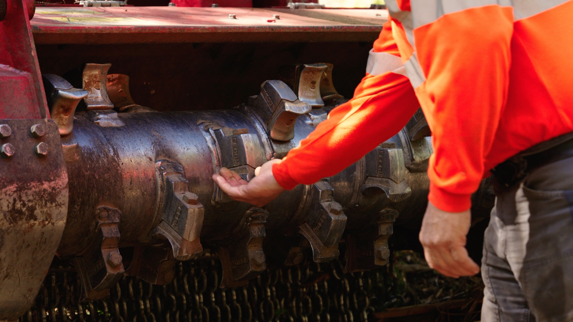 Closeup of a forestry mulcher drum with carbide teeth being inspected by a Premier Land Service crew member