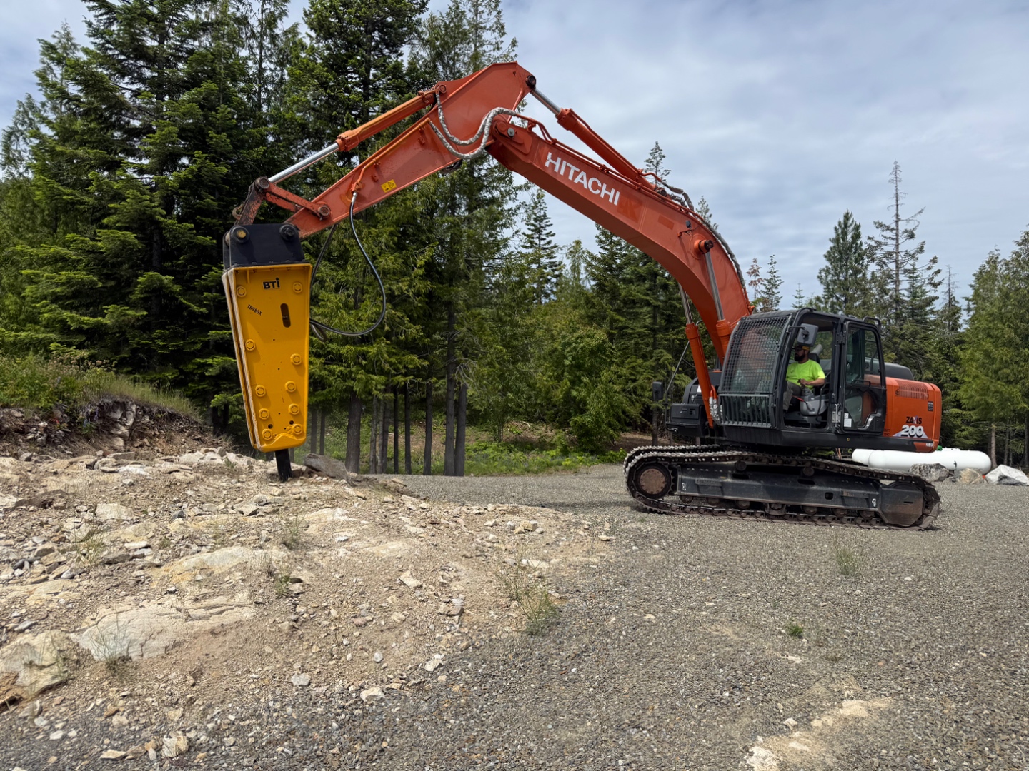 Premier Land Service excavator with hydraulic hammer breaking rock during Bonner County driveway prep