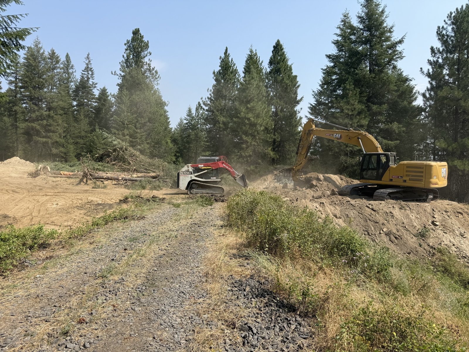 Compact track loader and excavator working together to clear timber and rough in a driveway on a 5-acre Sagle site